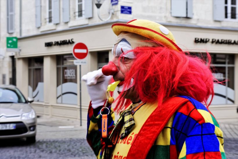 Melo le Clown rigolo Clown avec cheveux rouges et costume coloré, se tenant dans une rue.