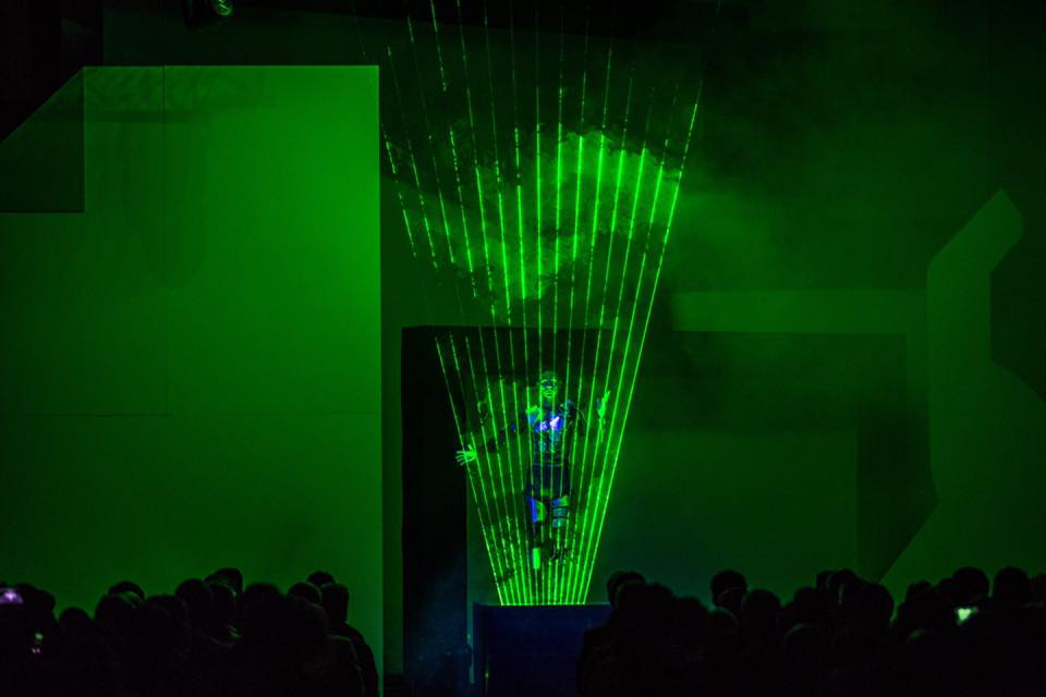 Theo Dari Un spectacle lumineux avec des lasers verts sur un fond sombre et une silhouette humaine.