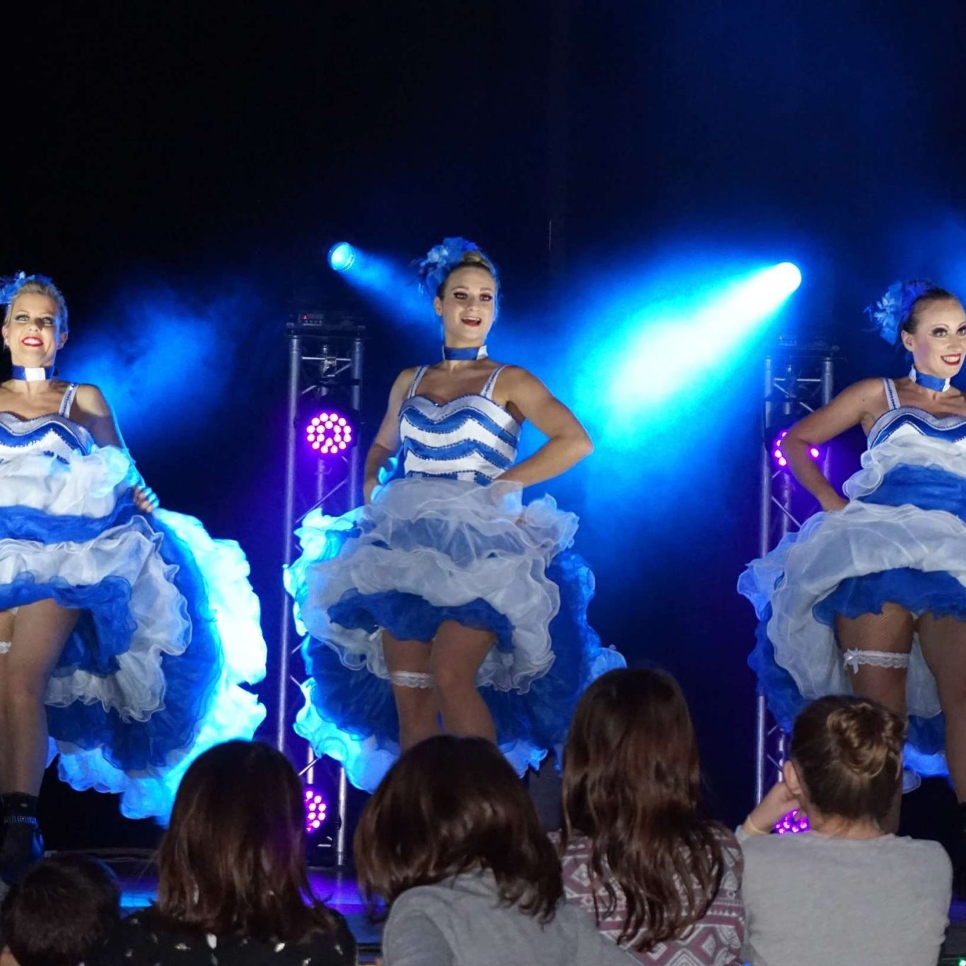 Danseuses en costumes bleu et blanc, performe sous des éclairages dynamiques.