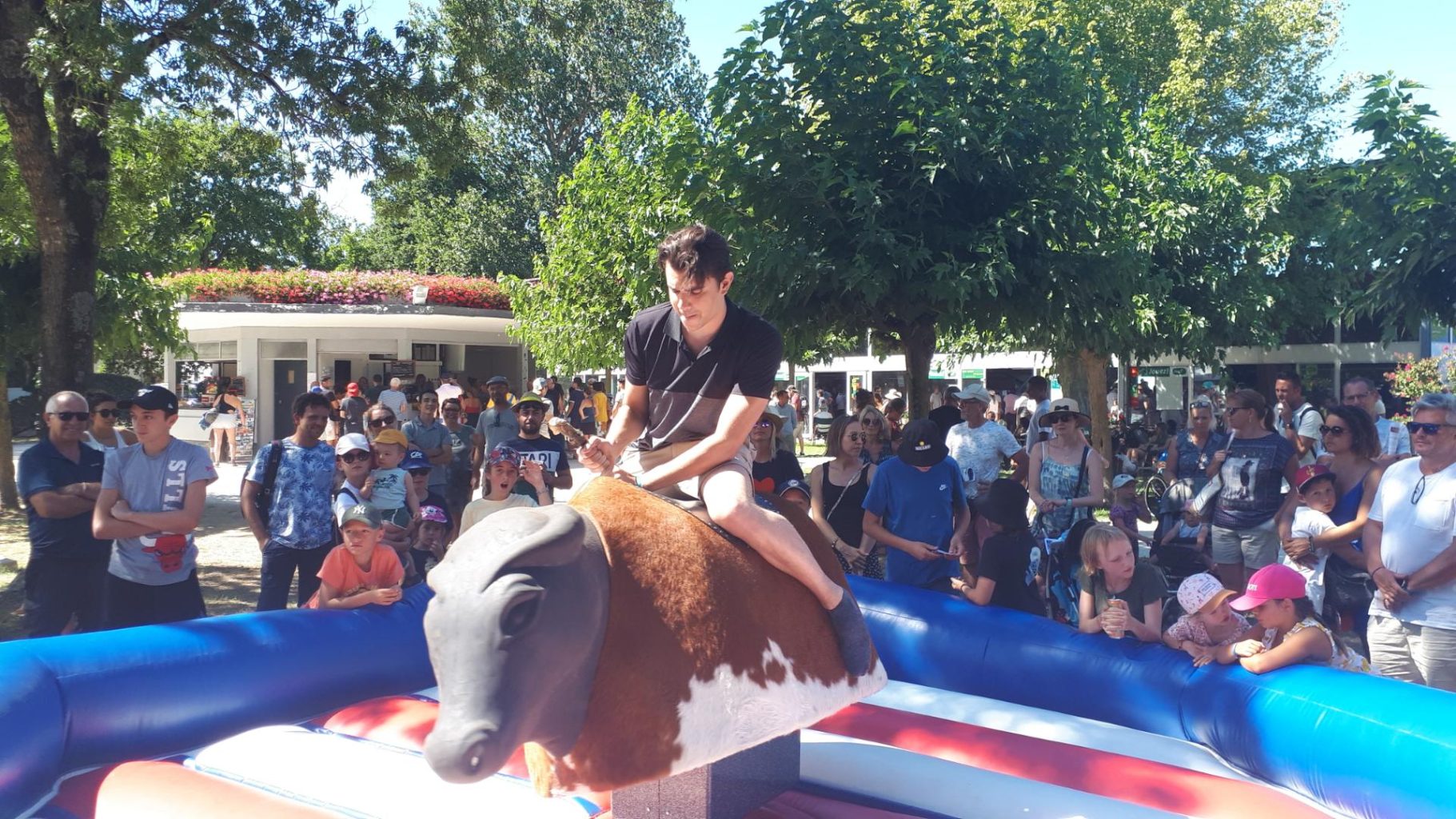 Taureau mécanique Un jeune homme monte un taureau mécanique lors d'un événement festif, entouré de spectateurs.